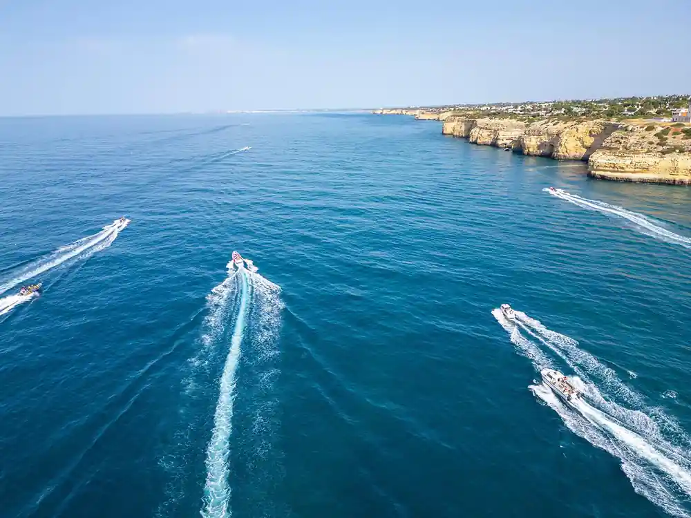 Boats crossing open blue water below a long cliff coastline