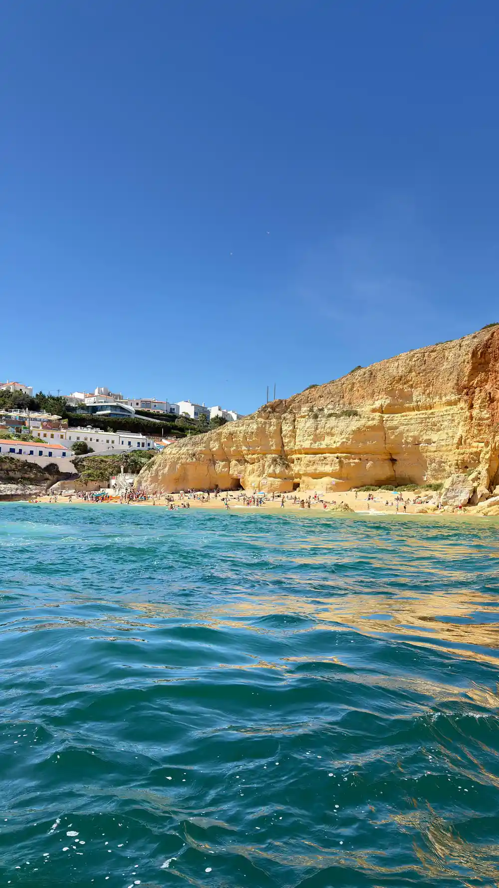 A busy beach below the cliffs with buildings on the top