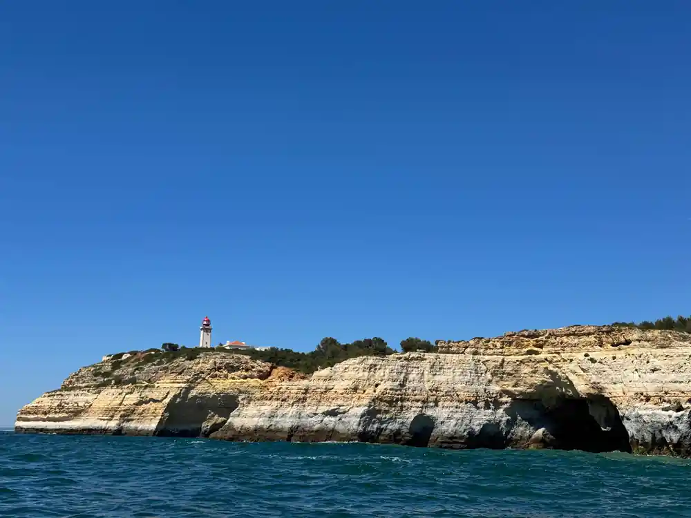 A lighthouse on the clifftop above a dark rock shoreline