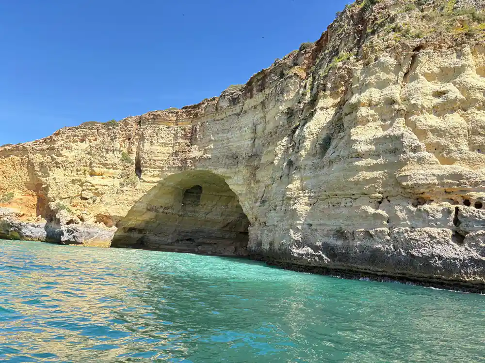 A pale cliff with a dark cave mouth above turquoise water