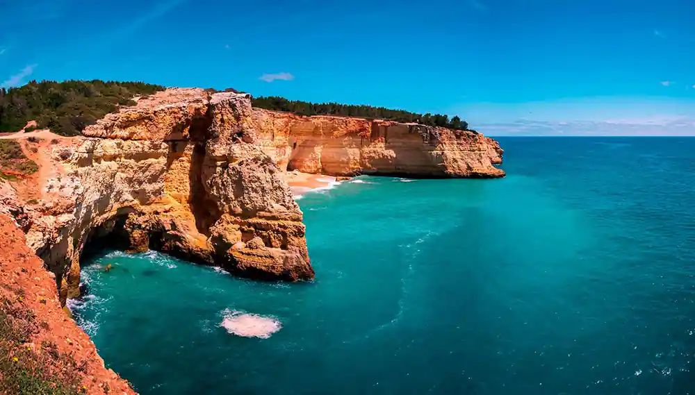 A red-brown cliff with an arch above a turquoise cove