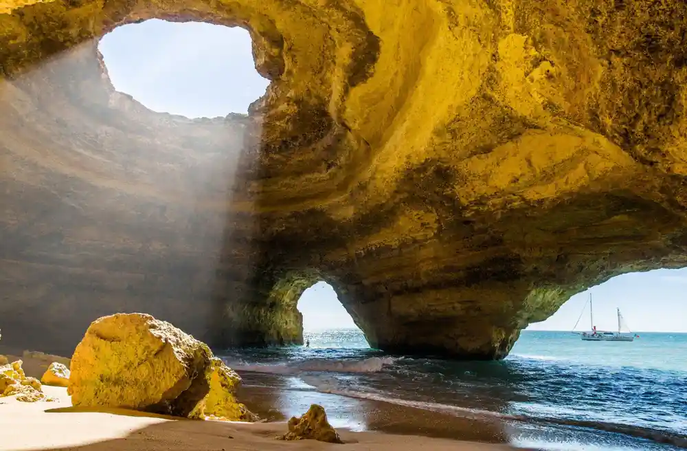 Sunlight striking the ribbed rock ceiling above a sandy cave floor