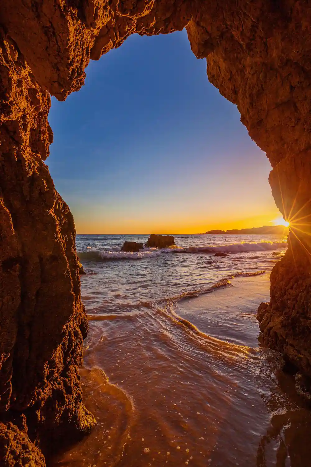 Sunrise seen through a cave mouth onto a wet beach