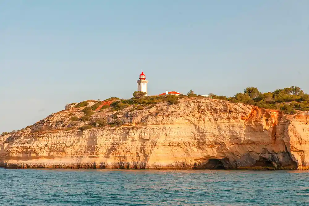 A white lighthouse on top of an orange cliff above the sea