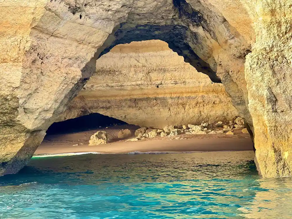 A wide pale rock arch over a sandy beach and clear shallows