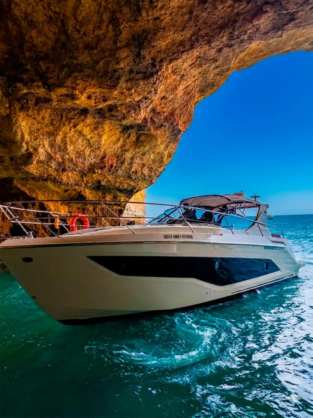 The yacht in bright sun beneath a curving rock roof
