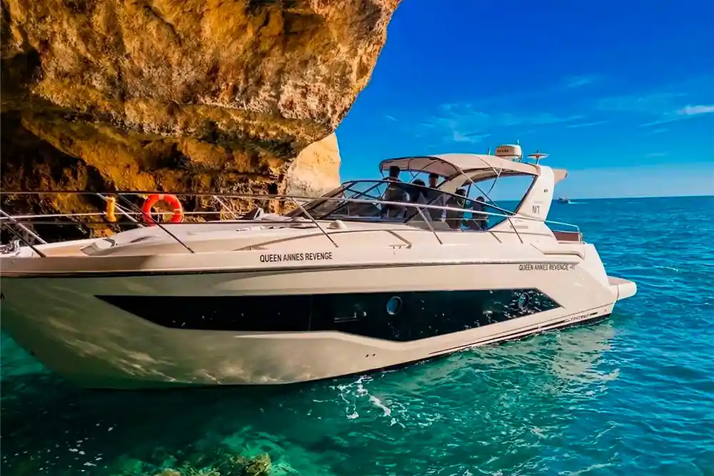 The yacht on green water beneath a natural rock arch