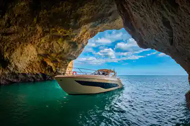 A yacht at the mouth of a sea arch on turquoise water