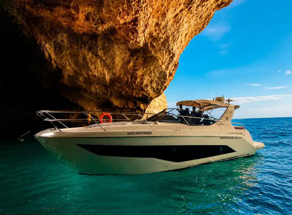 The yacht under a vaulted rock arch against a blue sky